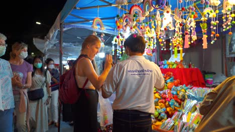 Young-female-traveler-haggling-with-old-asian-man-at-night-market
