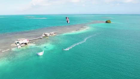Hombre-Kiteboard-Solo-En-Aguas-Azules-Mar-Caribe-Palafito-Los-Roques,-Tiro-De-Drones