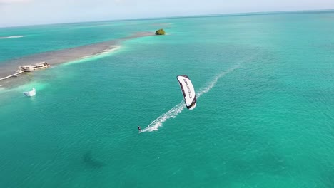 Aerial-view-MAN-have-fun-USING-WHITE-CORE-KITE-on-turquoise-caribbean-sea,-Los-Roques