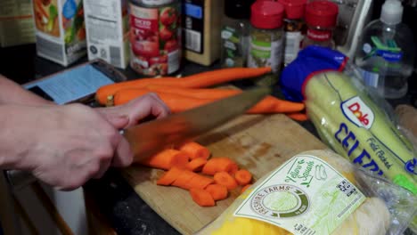 Mujer-Cortando-Con-Un-Cuchillo-Grande-Zanahorias-Naranjas-Largas-En-Una-Tabla-De-Madera-En-La-Cocina