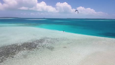 Drone-shot-Two-men-kitesurf-opposite-each-other,-meet-and-cross-on-kites-over-sea-on-turquoise-clear-crystal-water
