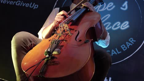 view-from-the-bottom-of-the-cello-up-to-the-musician,-a-young-Caucasian-man-with-short-hair,-head-turned-to-the-right,-on-a-bar-stage