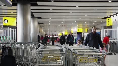 Reihe-Von-Gepäckwagen-Im-Flughafen-Heathrow-Terminal-3-Mit-Passanten