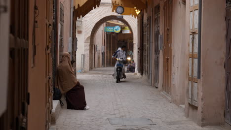 Establisher-shot-of-Marrakesh-street-with-woman-and-motorcycle-passing-by,-day