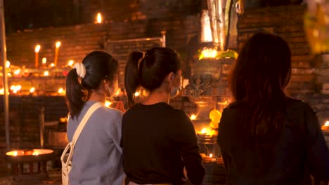 Rückseite-Von-Drei-Jungen-Frauen,-Die-Im-Buddhistischen-Tempel-Beten,-Beleuchtet-Mit-Kerzen