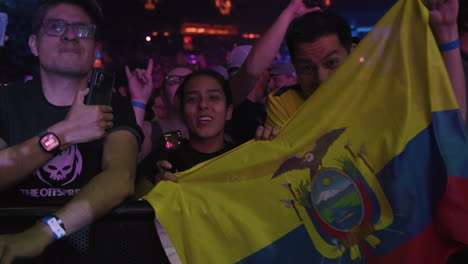 Joyful-Young-Spectators-Fans-Singing-Cheering-Holding-Ecuador-Flag-During-Music-Concert-Show-in-Arena,-Colorful-Spotlights-and-Audience-Crowd-Around