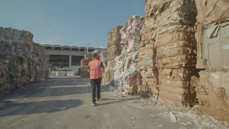 Trabajador-Caminando-Entre-Grandes-Pilas-De-Papeles-Listos-Para-Reciclar