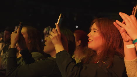 Young-Women-Ladies-Holding-Cell-Phones-Filming-and-Singing-During-Music-Concert-Show,-Audience-Crowd-in-Arena-Filming-Music-Performance-on-Stage
