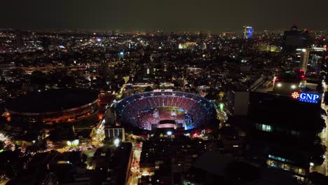 Aerial-view-around-the-Ciudad-de-los-deportes-venue,-flashing-during-concert-night-in-Mexico-city---circling,-drone-shot