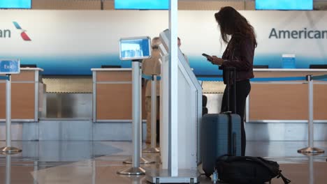 Lady-at-aeroport-interacting-with-kiosk-and-doing-check-in-and-preparie-her-checked-luggage-at-the-American-Airline-Ohair-airport-chicago