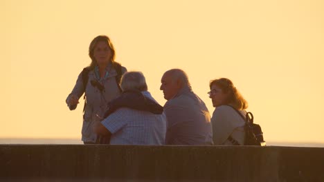 Gruppe-Alter-Seniorenfreunde,-Die-Goldenen-Sonnenuntergang-Am-Ozeanstrand-Sitzen