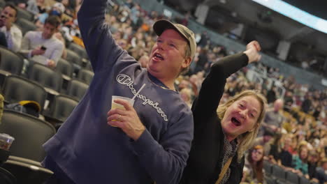 Joyful-Mid-Age-Couple-Spectators-Fans-Dancing-Arms-Up-Holding-Drink-Cup-During-Music-Concert-Show,-Enjoying-The-Event,-Arena-Stands-and-Audience-Crowd-Around