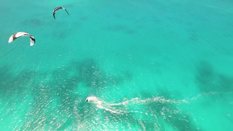 Drone-shot-two-men-kiteboarders-flying-opposite-each-other-on-kiteboards-over-the-sea,-Los-Roques