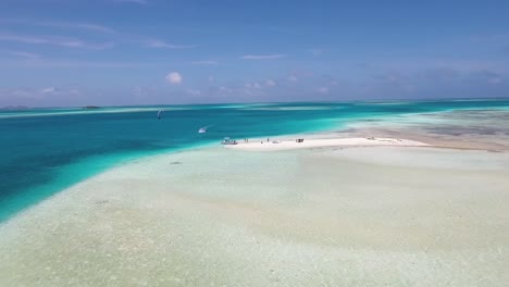 Aerial-approach-sandbank-with-people-enjoy-and-man-jump-kitesurfing,-los-roques