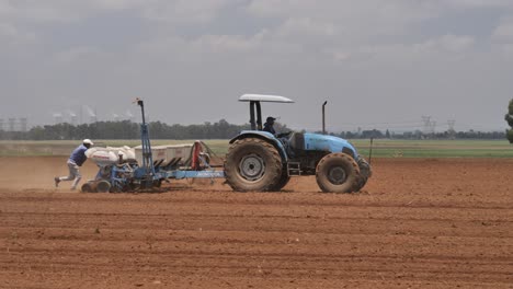 One-blue-tractor-plants-seeds-while-another-sprays-fertilizer-on-field