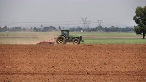Green-tractor-with-tine-harrow-tills-soil-in-agriculture-crop-field