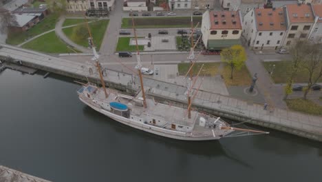 An-aerial-view-The-masted-sailing-ship-Meridian,-a-symbol-of-Klaipda,-is-moored-at-the-Danes-River-quays-in-a-autumn-day
