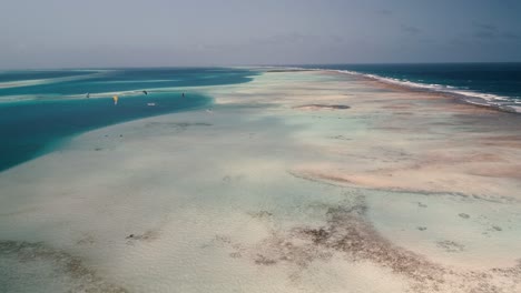 Drone-Shot-Barrera-De-Arrecife-Archipiélago-De-Los-Roques-Con-Kitesurfistas-En-El-Fondo,-Viajes-De-Aventura