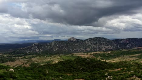 Dolly-out-aerial-drone-extreme-wide-shot-of-the-mountain-range-of-the-Pedra-de-Sao-Pedro-in-Sítio-Novo,-Brazil-in-the-state-of-Rio-Grande-do-Norte-during-a-overcast-stormy-summer-day