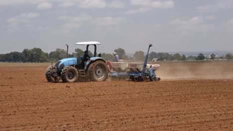 Using-tractor-and-seeder,-two-farmers-plant-agriculture-crop-in-field