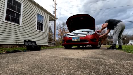 Time-Lapse-Shot-Of-Man-Fixing-His-Red-Car-In-Front-Of-His-Home,-Dog-Passing-Nearby