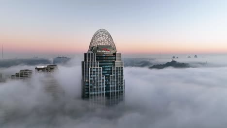 Aerial-view-approaching-the-fog-covered-Great-American-tower,-sunrise-in-Cincinnati,-USA---tilt,-drone-shot