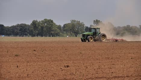 Heat-haze-and-dust-rise-from-crop-field-as-tractor-tows-tine-harrow
