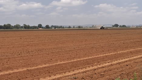 Distant-tractor-loosens-farmer's-field-top-soil-by-pulling-a-harrow