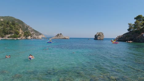 Toma-Panorámica-De-Turistas-Nadando-En-Las-Aguas-Tropicales-En-Parga,-Grecia