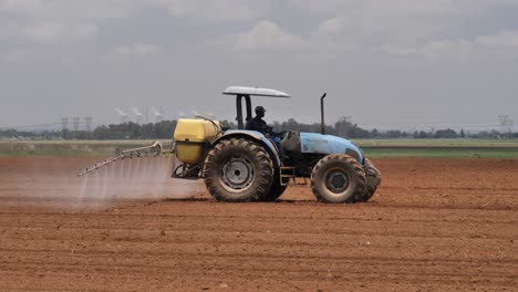 Farmer-in-old-blue-tractor-sprays-field-of-fresh-planted-crop-seeds