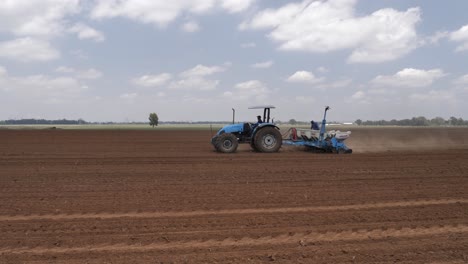 Blue-tractor-and-seed-planter-drive-across-field-of-fresh-tilled-soil