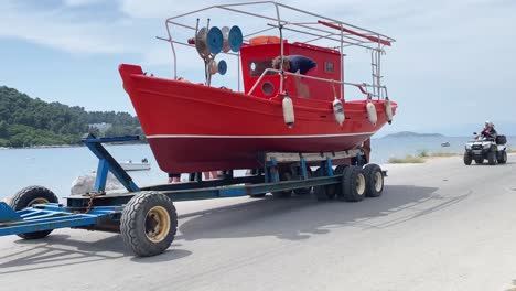 June-2022-Unidentified-Worker-Moving-A-Freshly-Painted-Red-Boat-on-Skiathos-Greek-Island-In-The-Sunshine-With-Quad-Bike-Following