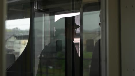 Blick-Durch-Das-Reflektierende-Glas-Des-Gähnenden-Japanischen-Zugführers,-Der-Aus-Dem-Fenster-Schaut