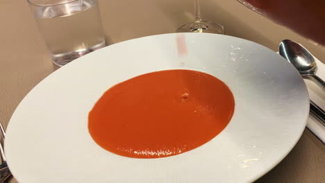 Tomato-soup-is-poured-onto-a-plate-with-a-spoon-and-a-table-with-no-people