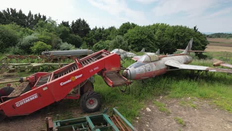 Rusty-farming-equipment-and-hunting-jet-Provost-fuselage-low-aerial-orbit-view-across-private-farmland