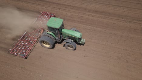 Aerial:-Dust-rises-as-tractor-pulls-spring-harrow-through-field-soil