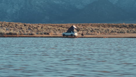 Roof-top-tent-on-car-next-to-fresh-water-lake-in-California-nature,-aerial