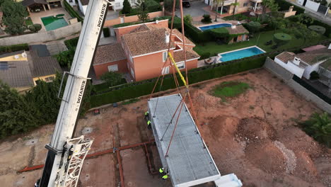 Aerial-lowers-down-big-crane-reveals-operators-working-with-hanging-home-module