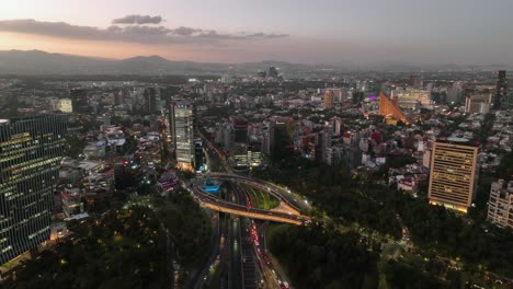 Aerial-view-around-the-Petroleos-Fountain,-dusk-on-Reforma-avenue,-in-Mexico-city---circling,-drone-shot