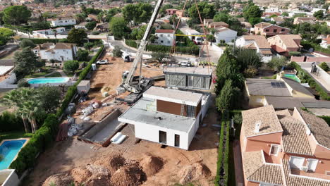 Crane-lifts-modern-modular-home-structure-at-construction-site,-aerial-view