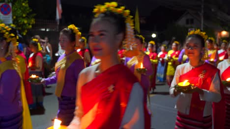Traditional-Thai-women-holding-candles-walking-in-front-of-camera,-smiling