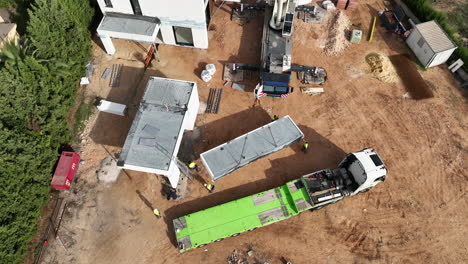Looking-down-at-crane-installing-modular-home-units-to-construction-site-aerial-view