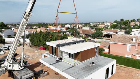 New-modern-home-being-put-in-place-by-crane-in-construction-site,-aerial-view