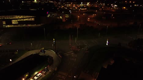 Night-flying-orbiting-UK-town-highway-with-illuminated-street-lights-and-McDonalds-advertising-logo-aerial-view