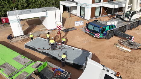 Operators-working-on-modular-home-construction-site,-aerial-drone-pan,-day