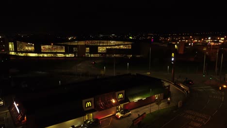 Cars-queue-at-McDonalds-fast-food-drive-through-at-night-in-Northern-UK-town-aerial-rising-view