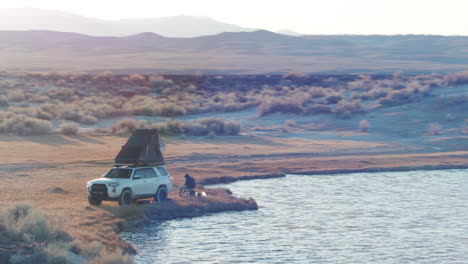 Back-country-camping-next-to-lake-with-roof-top-tent-on-car,-aerial