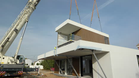 Contractors-assembling-modern-modular-housing-construction-suspended-by-crane-on-real-estate-site
