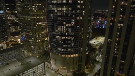 Aerial-view-away-from-the-illuminated-Brava-luxury-residence-in-Houston,-USA---rising,-pull-back,-drone-shot