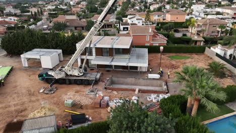 Aerial-circling-around-modular-building-home-construction-site-with-huge-crane